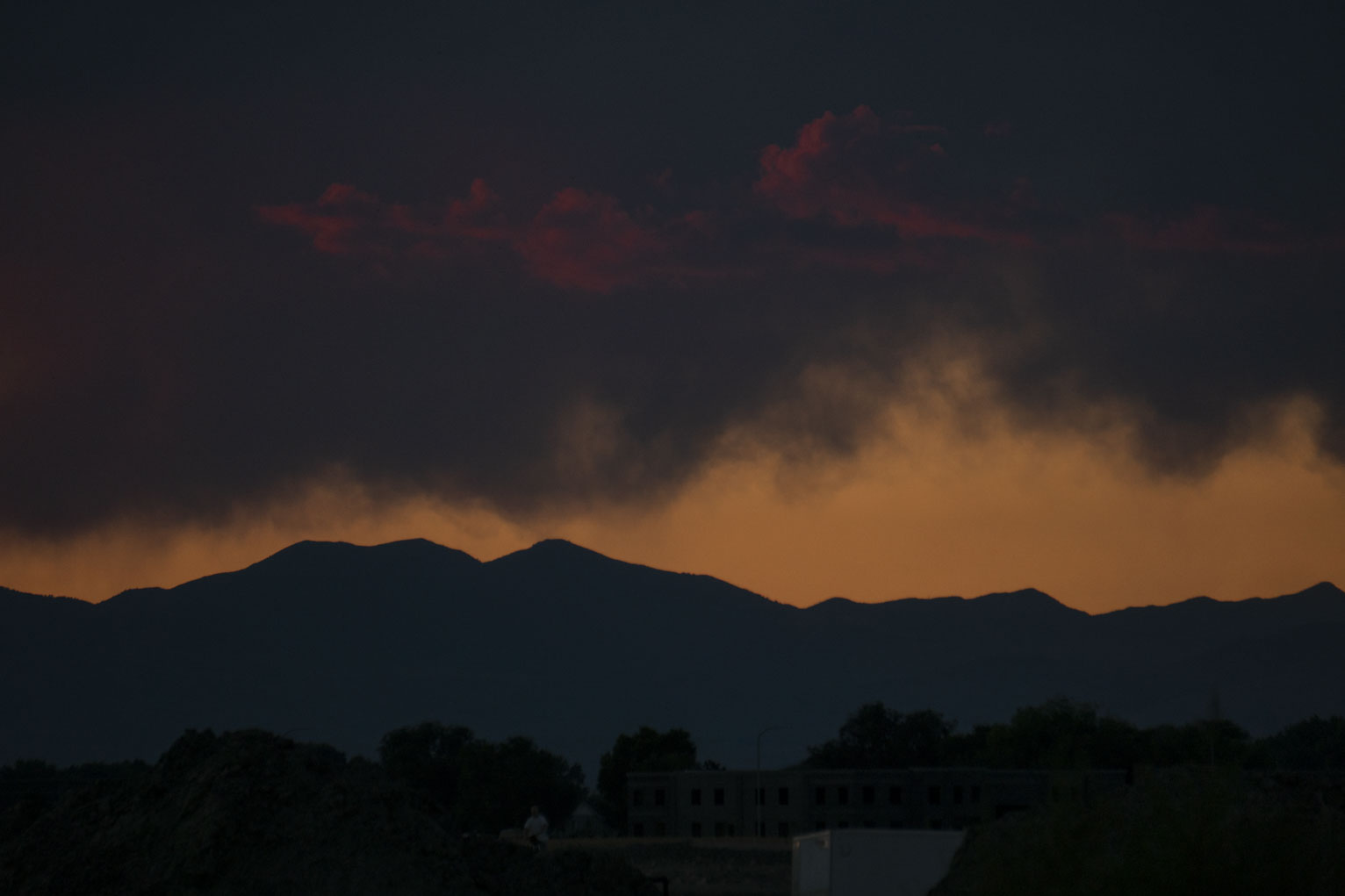 Fading red clouds above orange sky above mountains above trees